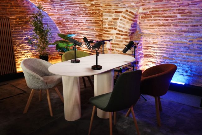 Quatre chaises colorées devant le mur de briques rouges de La Voûte Studio à Toulouse, studio réservé en créneau récurrent pour tenir un planning de création de contenu podcast